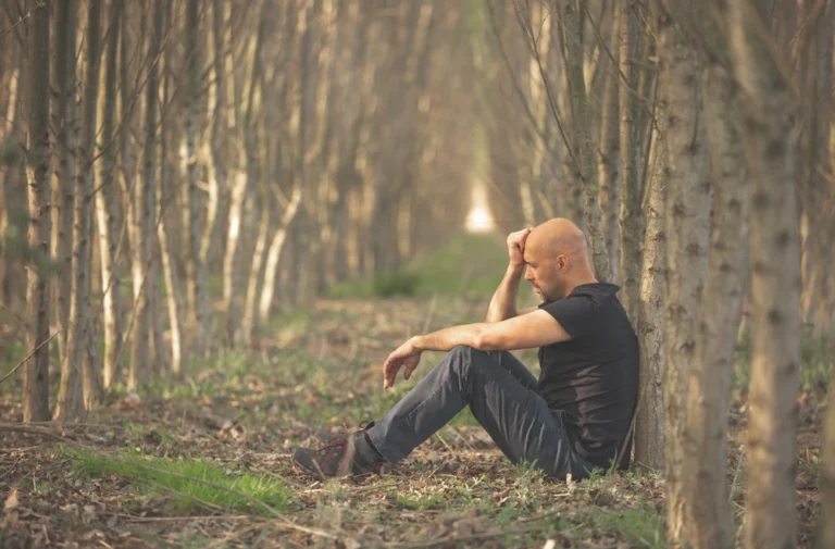Man zit moedeloos tegen boom in bos; beeld symboliseert depressie of burn-out door onveilige hechting