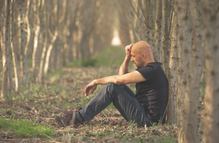 Man zit moedeloos tegen boom in bos; beeld symboliseert depressie of burn-out door onveilige hechting
