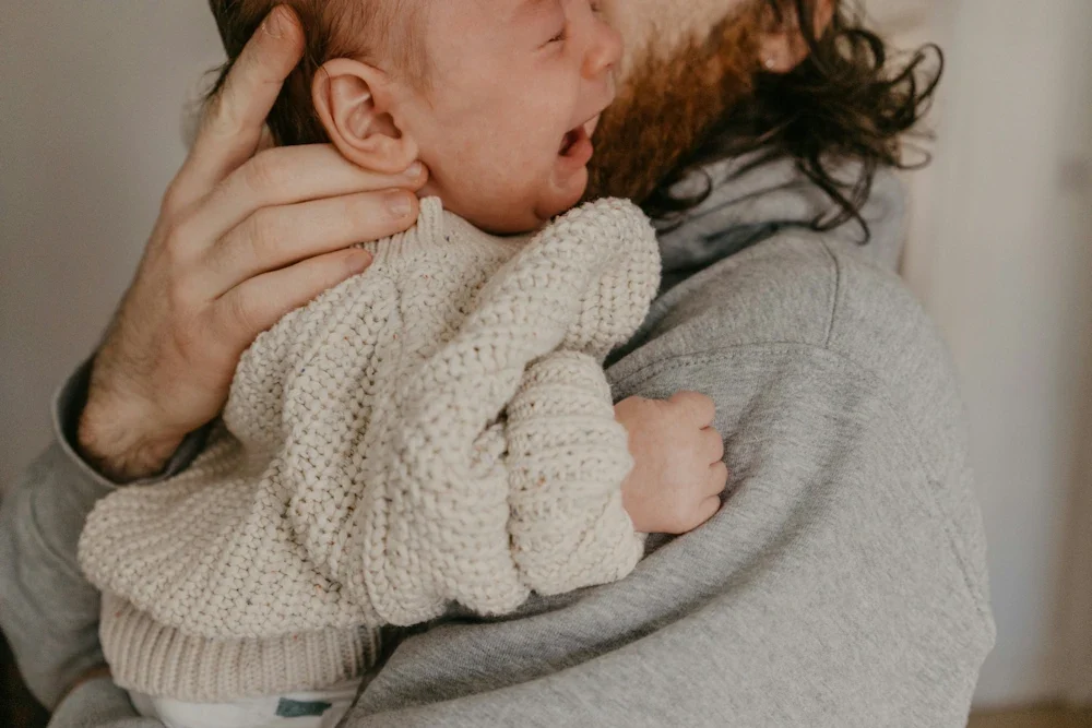 Vader houdt huilende baby troostend tegen zich aan, illustreert helpen bij reguleren van emoties
