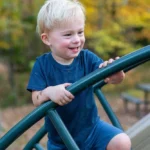 Lachend jongetje klimt geconcentreerd op klimrek, illustreert zelfvertrouwen ontwikkelen door uitdagingen aan te gaan